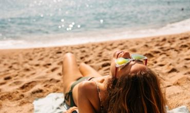 Femme en maillot vert bronzant sur la plage, mer visible derrière – petit format 248×416.