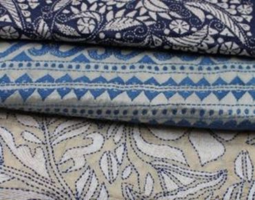 Tissu avec des motifs de broderie détaillés dans des tons bleus et beiges, avec des designs floraux et géométriques.