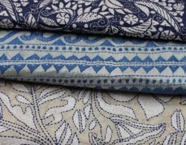 Tissu avec des motifs de broderie détaillés dans des tons bleus et beiges, avec des designs floraux et géométriques.