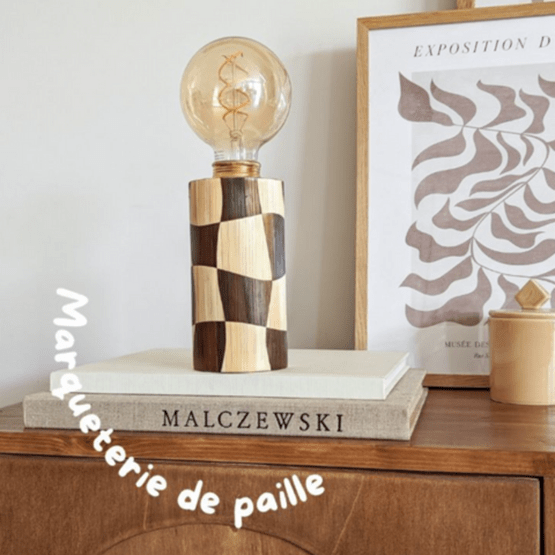 Lampe en marqueterie de paille posée sur une pile de livres, dans un décor vintage.