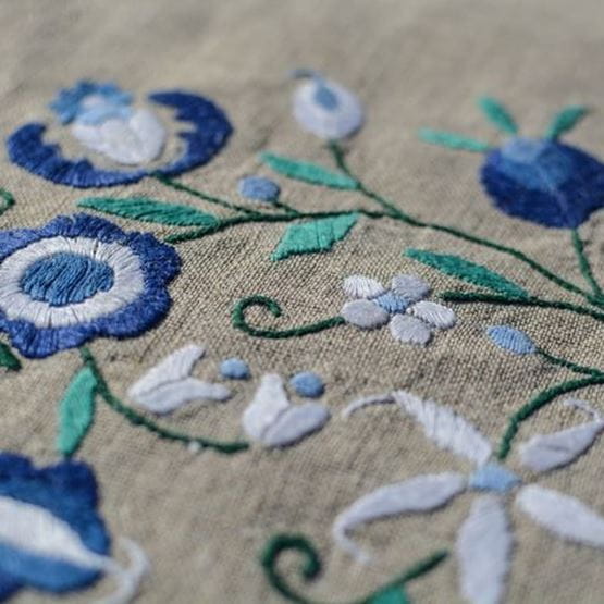 Motif brodé floral bleu sur toile beige, point de tige visible