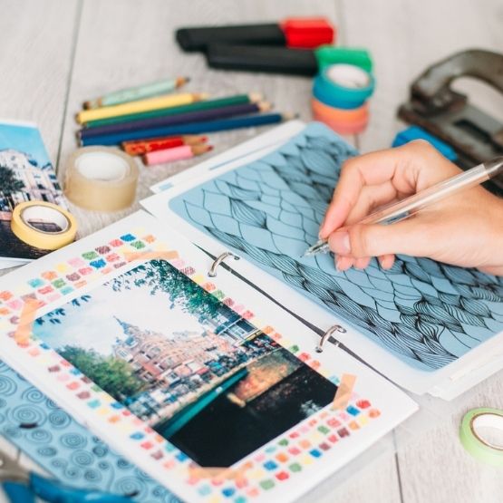 Main dessinant dans un carnet de scrapbooking avec photo décorée de rubans adhésifs colorés.