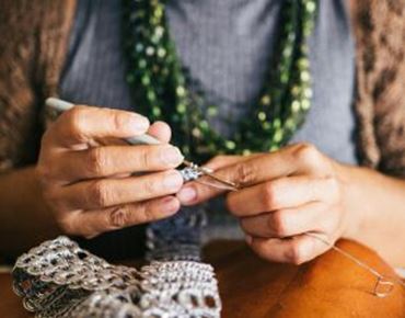Mains en train de crocheter avec un fil métallisé argenté, sur une table en bois.