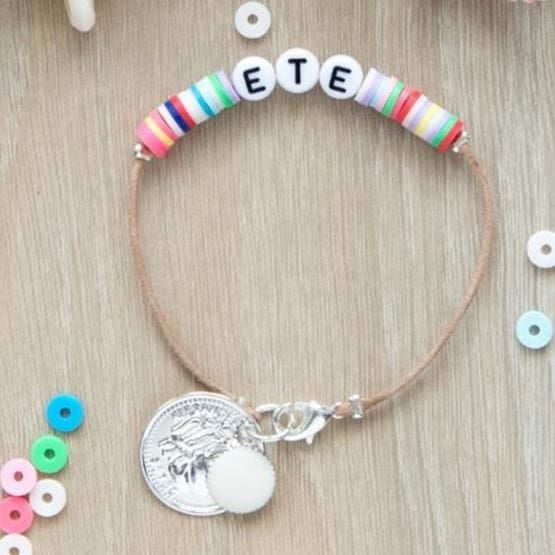 Bracelet d’été fait main avec des perles heishi colorées, lettres formant “ÉTÉ” et pendentifs argentés.