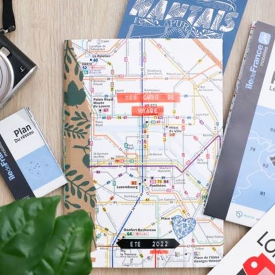 Carnet de voyage personnalisé posé sur un plan de métro parisien, entouré de guides et d’accessoires touristiques.