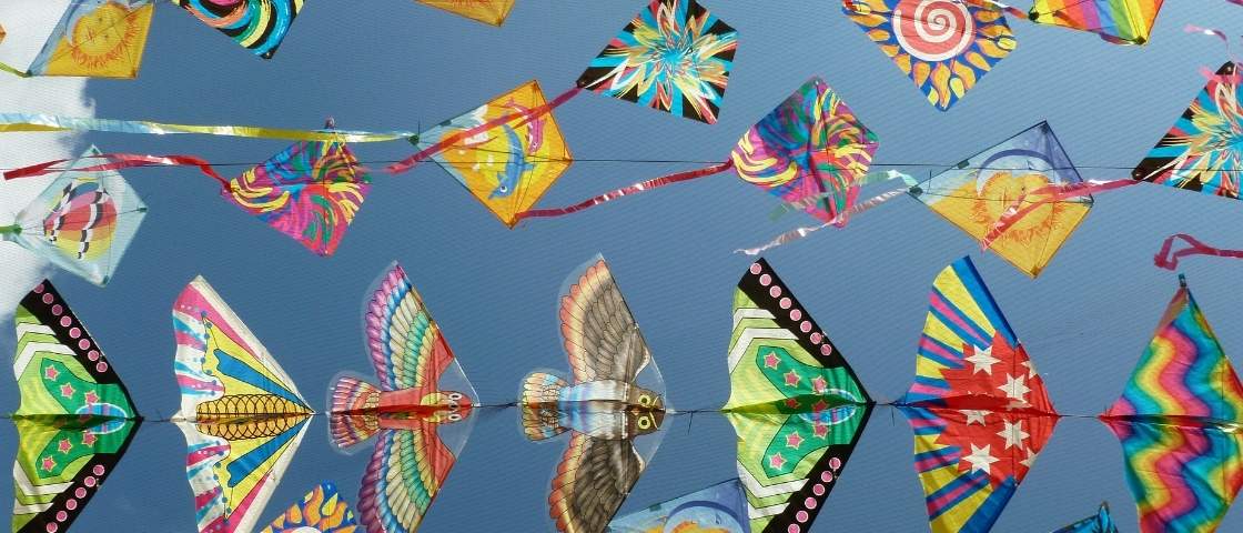 Cerfs-volants colorés en forme de losange flottant dans un ciel bleu lors d’un festival.
