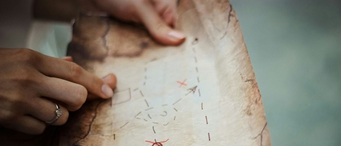 Mains d’un enfant pointant une carte au trésor dessinée à la main avec des repères.