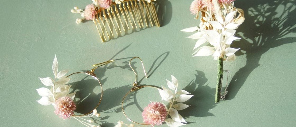 Ensemble de bijoux et accessoires en fleurs séchées, comprenant boucles d’oreilles, peigne et boutonnière, sur fond vert.