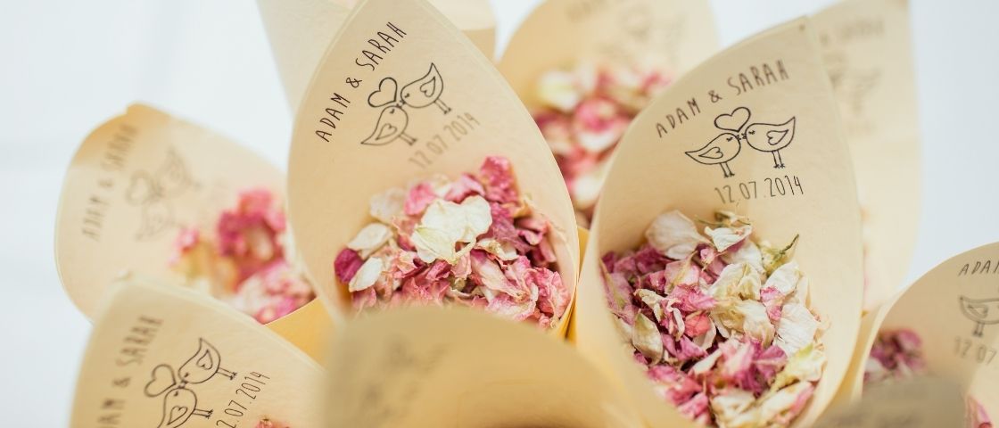 Cornets en papier personnalisés remplis de pétales de rose séchés pour une cérémonie de mariage.
