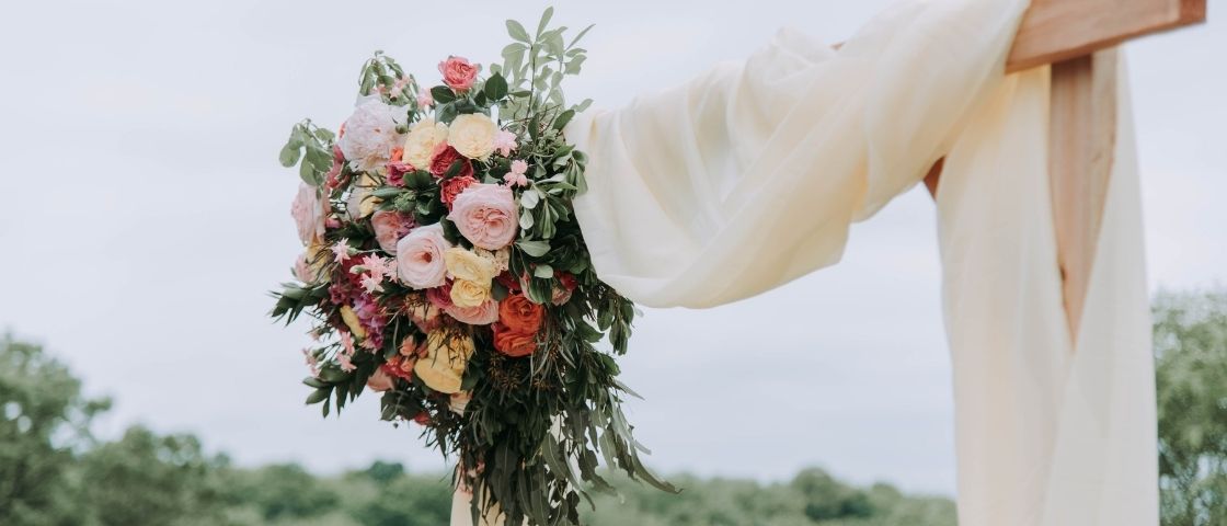 Arche fleurie de mariage avec un drapé blanc et un grand bouquet de fleurs pastel.