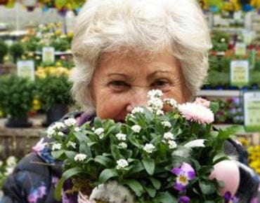 Femme âgée souriante tenant un bouquet de fleurs printanières dans une jardinerie.