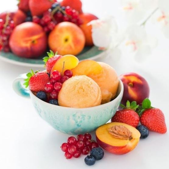 Coupe de sorbet à la pêche accompagnée de fruits rouges et de myrtilles fraîches.