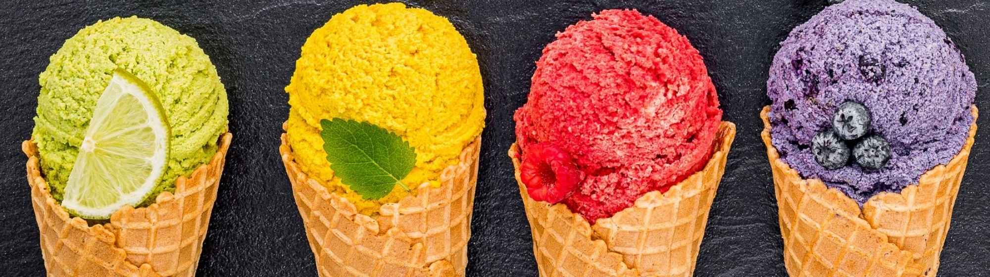 Quatre cornets de sorbet colorés avec des fruits assortis sur fond noir.