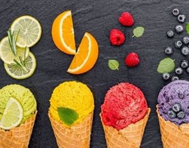 Quatre cornets de sorbet colorés avec des fruits assortis sur fond noir.