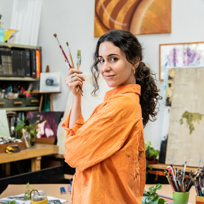 femme vêtue d'orange, regardant vers nous, avec des pinceaux dans les mains